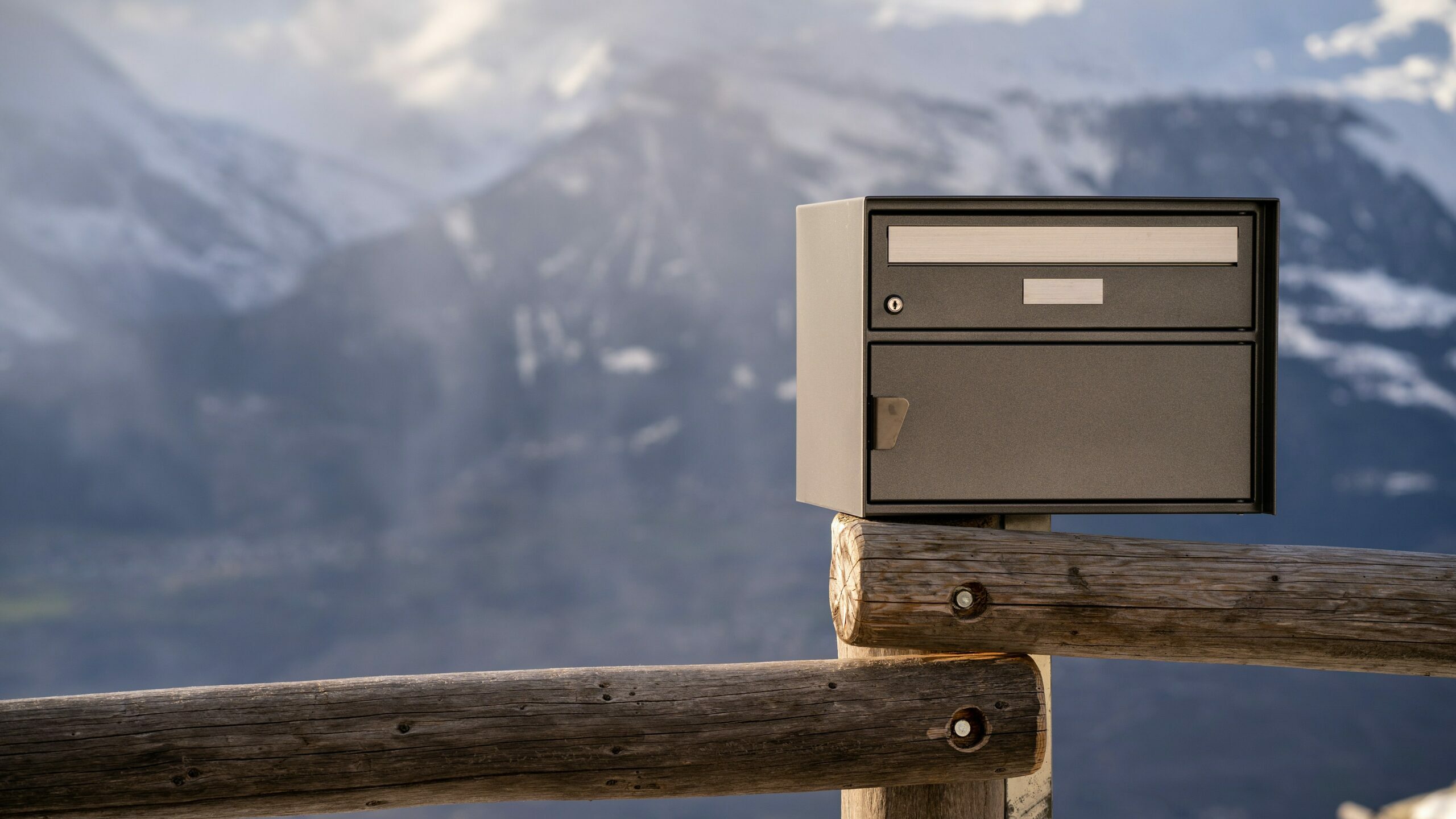 Ein Briefkasten steht auf einem Zaun vor einer Bergkulisse.