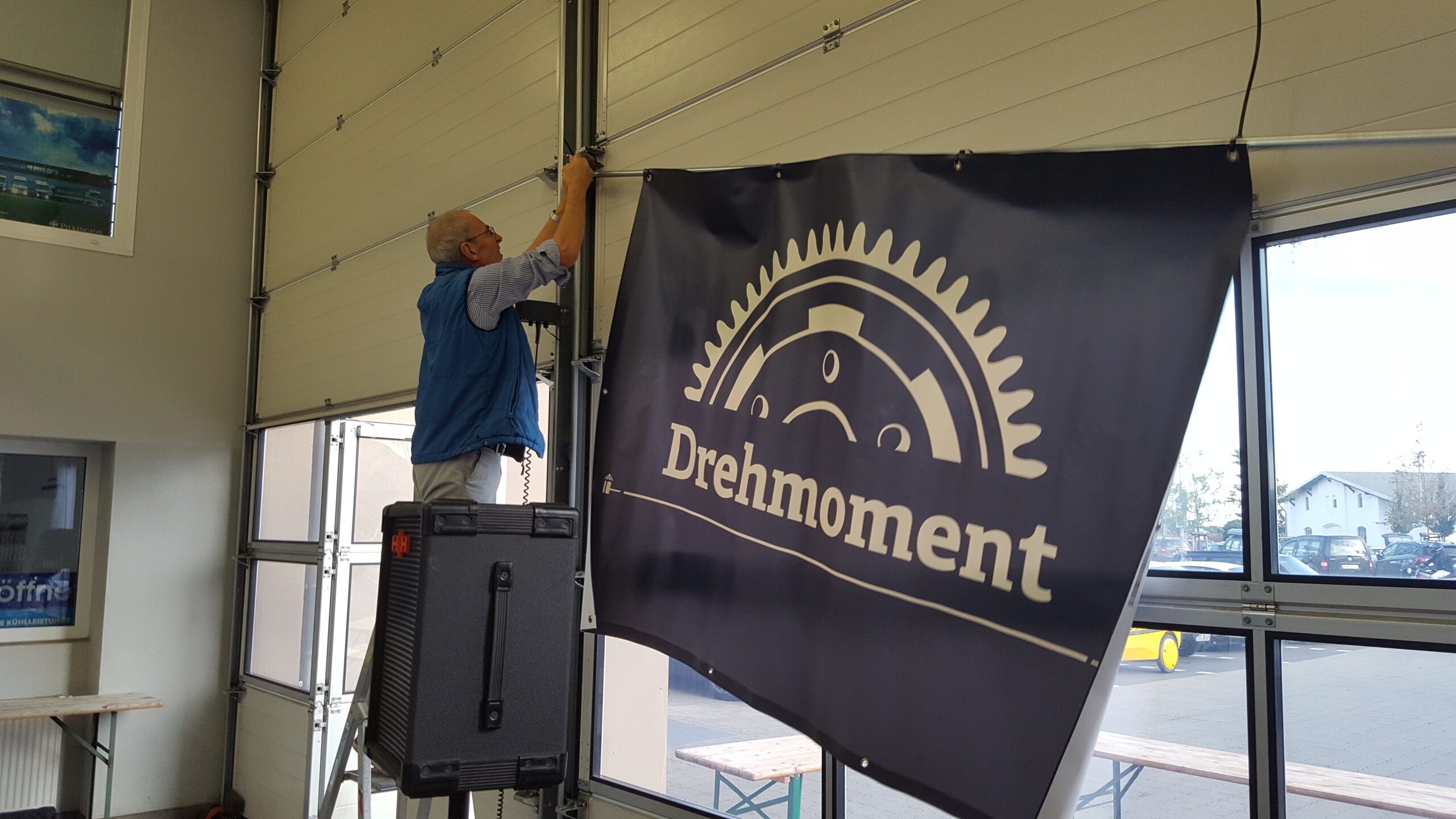 Mann hängt in Werkstattein "Drehmomente"-Banner auf